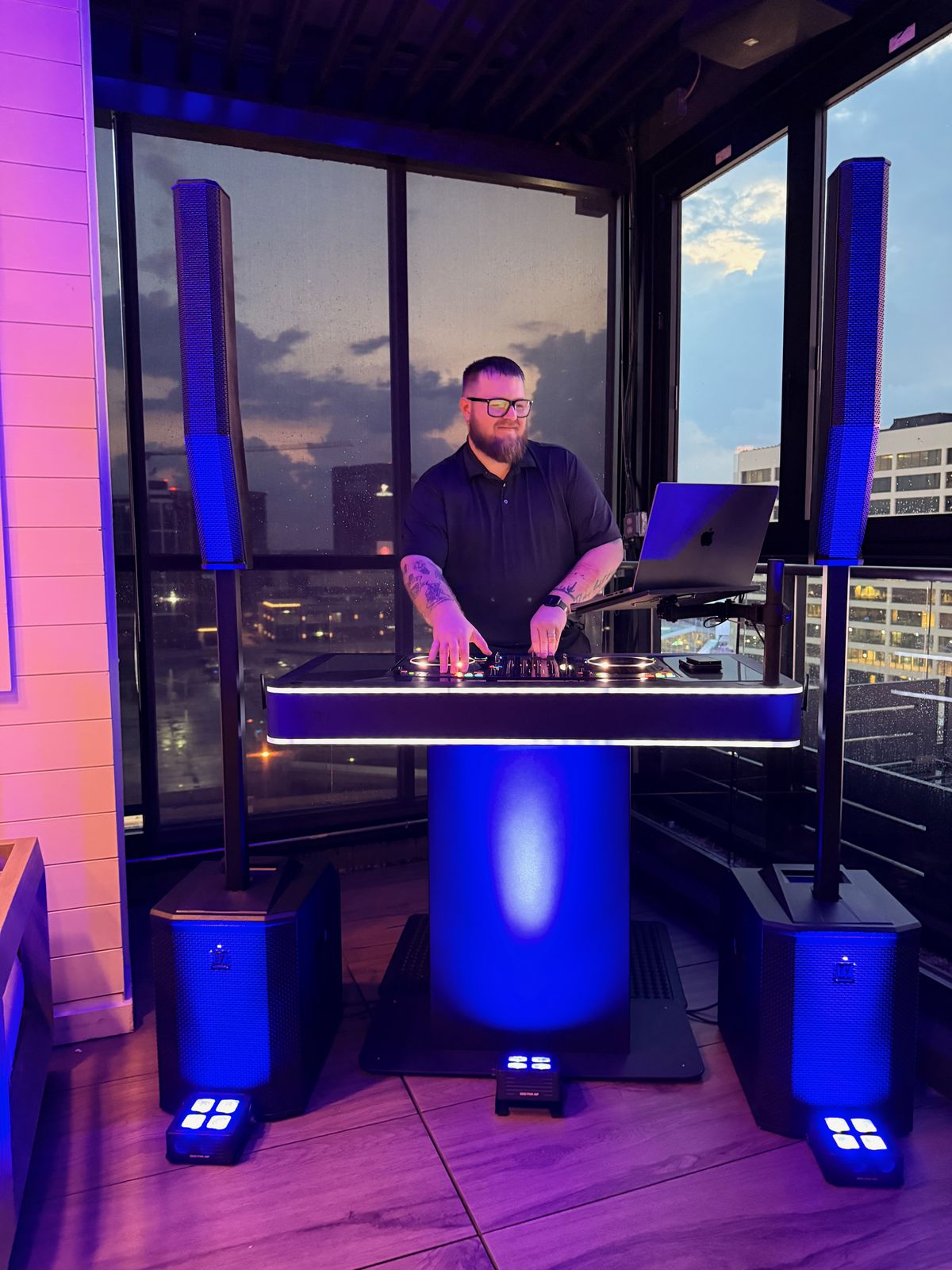 Tyler at his DJ booth with a city skyline at dusk